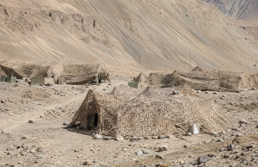 Highland desert field camp concealed with terrain-colored camouflage nets