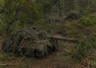 Armored equipment hidden with full-spectrum camouflage netting in hilly forest terrain