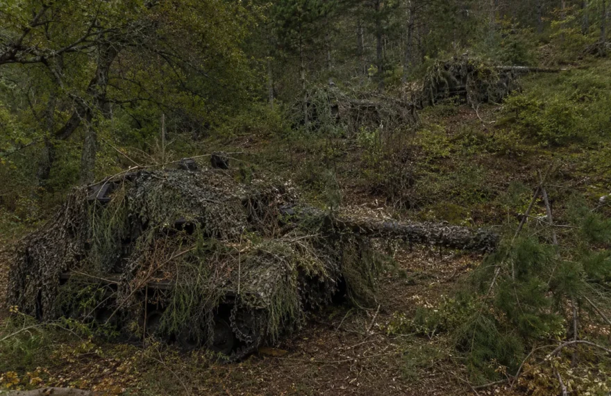 Armored equipment hidden with full-spectrum camouflage netting in hilly forest terrain