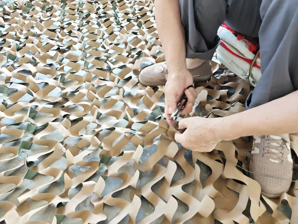 Workers attaching decorative pieces to a camouflage support net